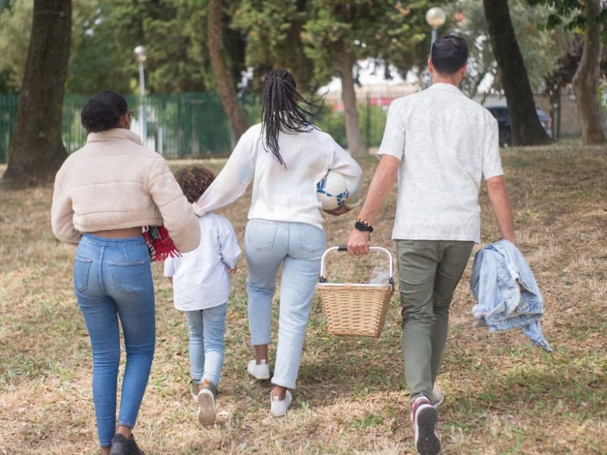 Family walking together carrying picnic basket in a sunny park.